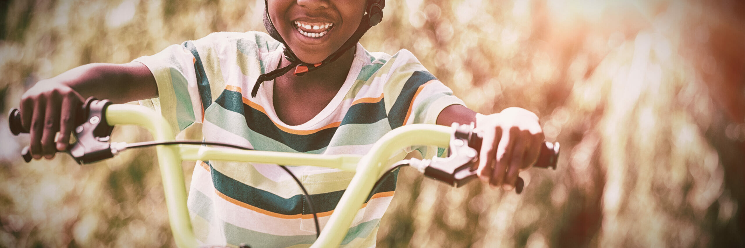 A little boy smiling, wearing a bicycle helmet, riding a bicycle